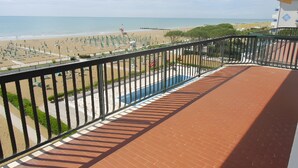 Uma varanda com vista para uma praia, uma piscina e um cais.