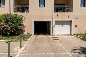 Une entrée d’immeuble avec une allée bordée de grilles, un petit jardin avec des fleurs roses et un balcon bien visible.