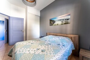 Une chambre à coucher avec une t ête de lit en bois, une couvre-lit matelassée, un tableau représentant une scène de plage et une porte donnant sur une autre pièce.