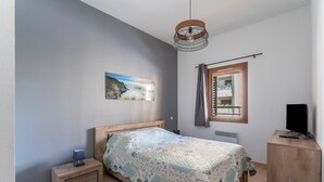 A bedroom with a bed, bedside table, lamp, TV, window, and a picture on the wall. - Apartment 'Appartement Des Cedres' with Shared Pool, Wi-Fi and Air Conditioning (Uzès)