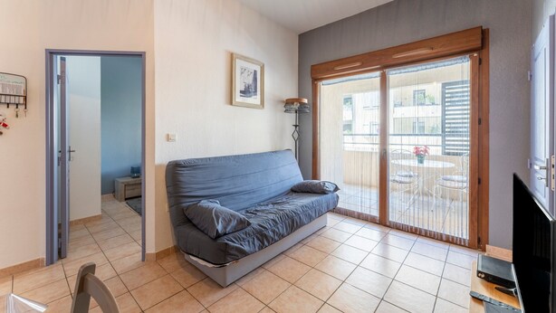 Een woonkamer met een bank, een televisie en een schuifdeur naar een buitenruimte.