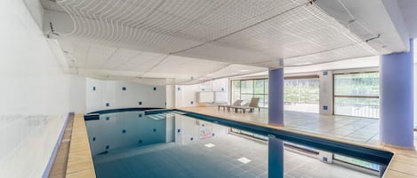 En swimmingpool med ett kaklat golv, ett tak med ett rutmönster och en sittgrupp med stolar och ett bord.