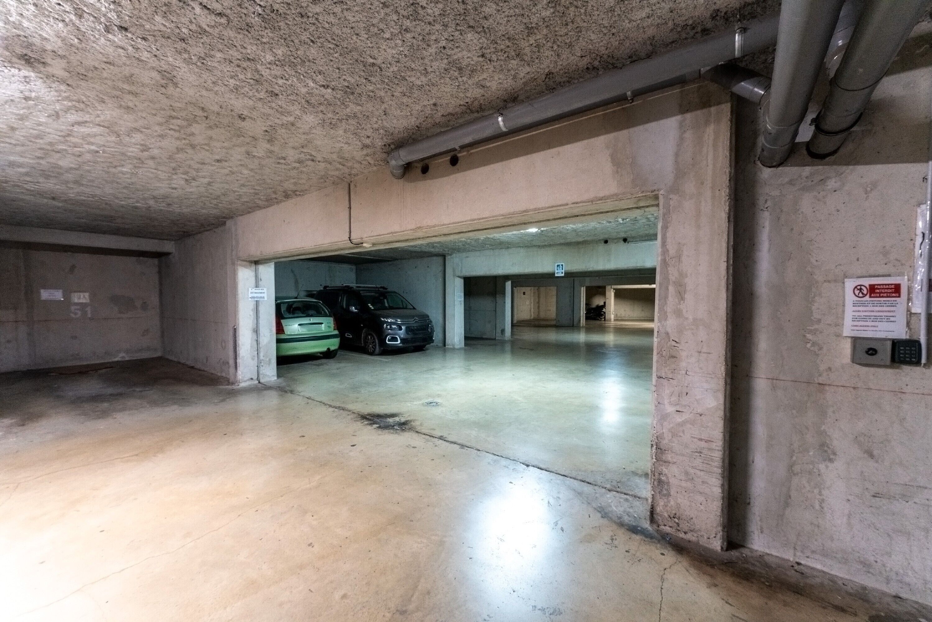 Un parking avec des murs en béton et une voiture verte garée à l’intérieur.