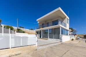 Une maison moderne à deux étages, dotée d’un balcon, d’un garage et d’une allée bordée d’une clôture.