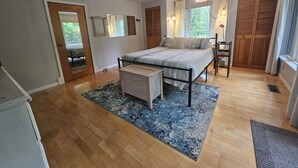 A bedroom with a bed, a nightstand, a wooden floor, a window with curtains, and a door. - Peaceful AuSable River Retreat-Frederic, MI Sleeps 6 (Frederic)