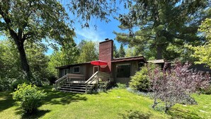 A two-story house with a red roof, a brick chimney, and a front porch with steps. - Peaceful AuSable River Retreat-Frederic, MI Sleeps 6 (Frederic)