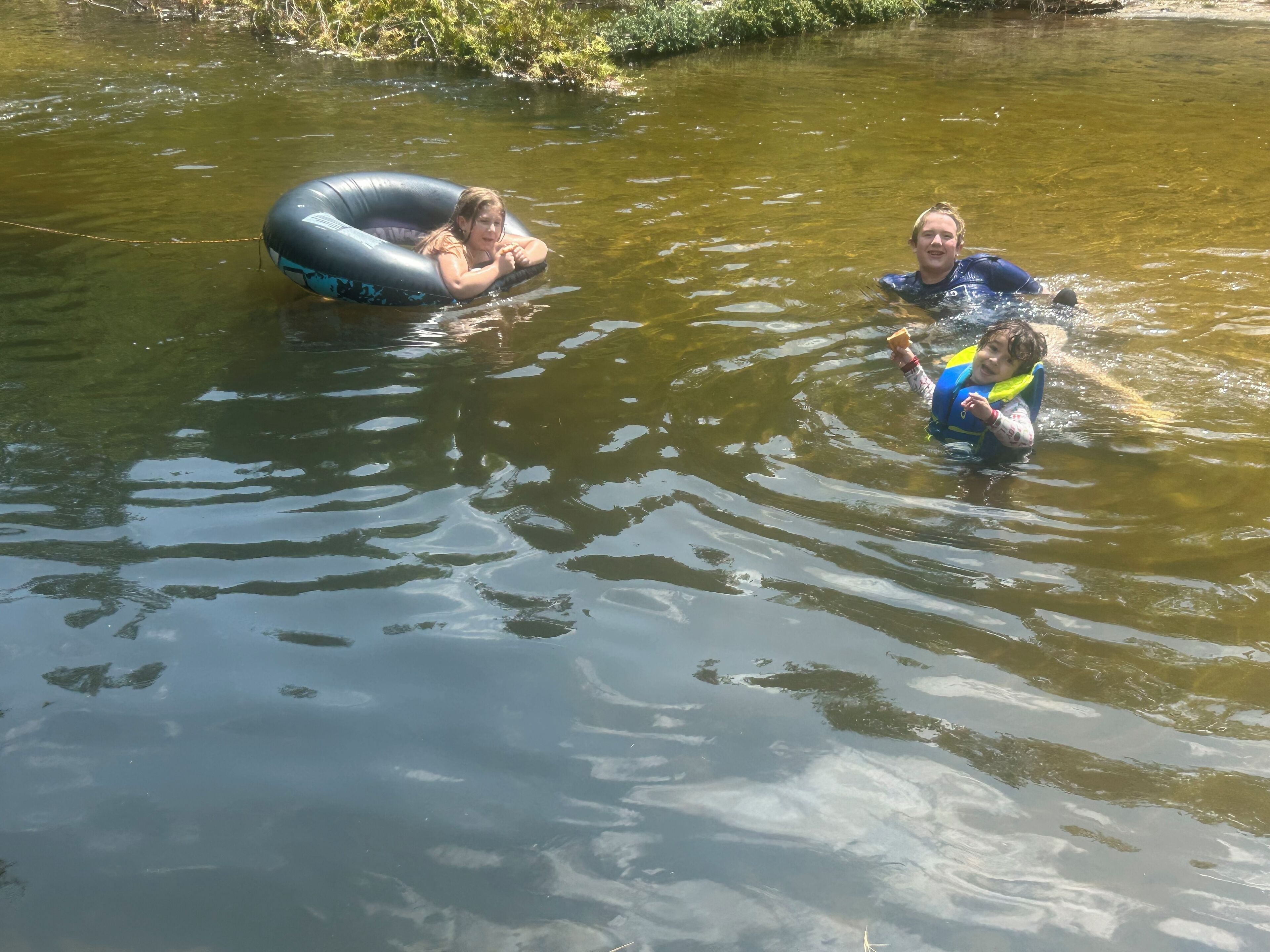 Two people floating in a river, one in an inflatable ring and the other in a life jacket.