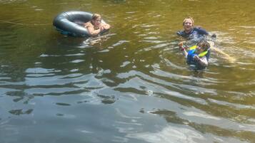 Two people floating in a river, one in an inflatable ring and the other in a life jacket.