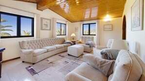 Una sala de estar con techo de madera, ventanas grandes, un conjunto de sofá y una lámpara.