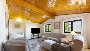Una sala de estar con techo de madera, un ventanal grande, un televisor de pantalla plana y un sofá.
