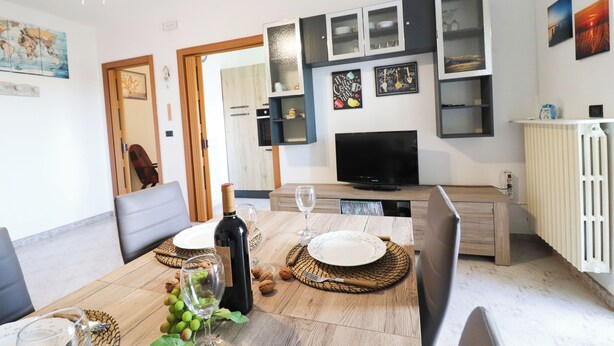 A dining area with a wooden table set for two, a television, and wall-mounted cabinets. - Surya's House Otranto (Otranto)