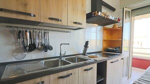 A modern kitchen with wooden cabinets, a stainless steel sink, and various utensils hanging on the wall. - Surya's House Otranto (Otranto)