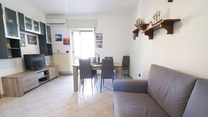 A living room with a sofa, TV, entertainment unit, dining table with chairs, and a kitchen area in the background. - Surya's House Otranto (Otranto)
