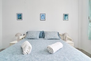A bed with a patterned bedspread, two pillows, two bedside lamps, and three framed pictures on the wall.
