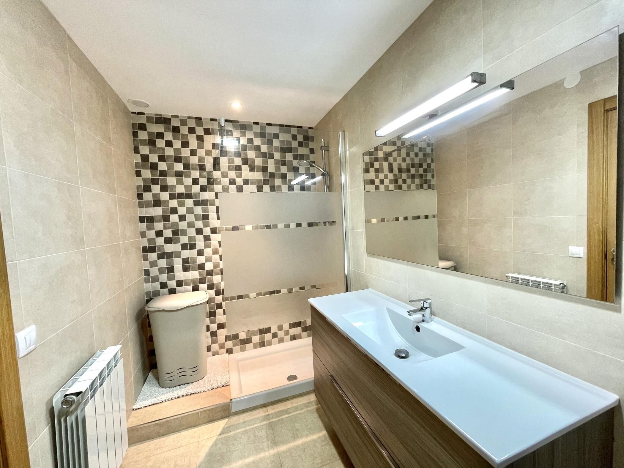 A modern bathroom with a large mirror, a white sink, and a shower area.