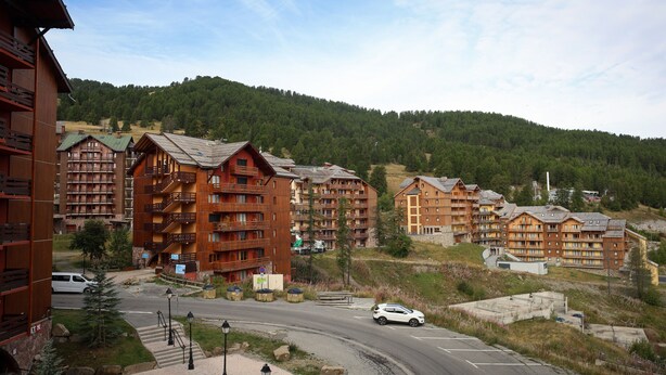 A mountain resort with multi-story wooden buildings, a road, and a forested hill in the background. - Apartment 'Appartemment 6 Couchages Risoul' with Mountain View and Balcony (Risoul)