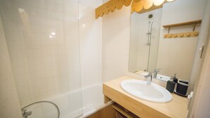 A bathroom with a bathtub, a sink, a mirror, and a wooden shelf. - Apartment 'Appartemment 6 Couchages Risoul' with Mountain View and Balcony (Risoul)