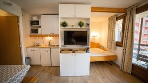 A compact room with a kitchenette, a bed, and a window with curtains. - Apartment 'Appartemment 6 Couchages Risoul' with Mountain View and Balcony (Risoul)