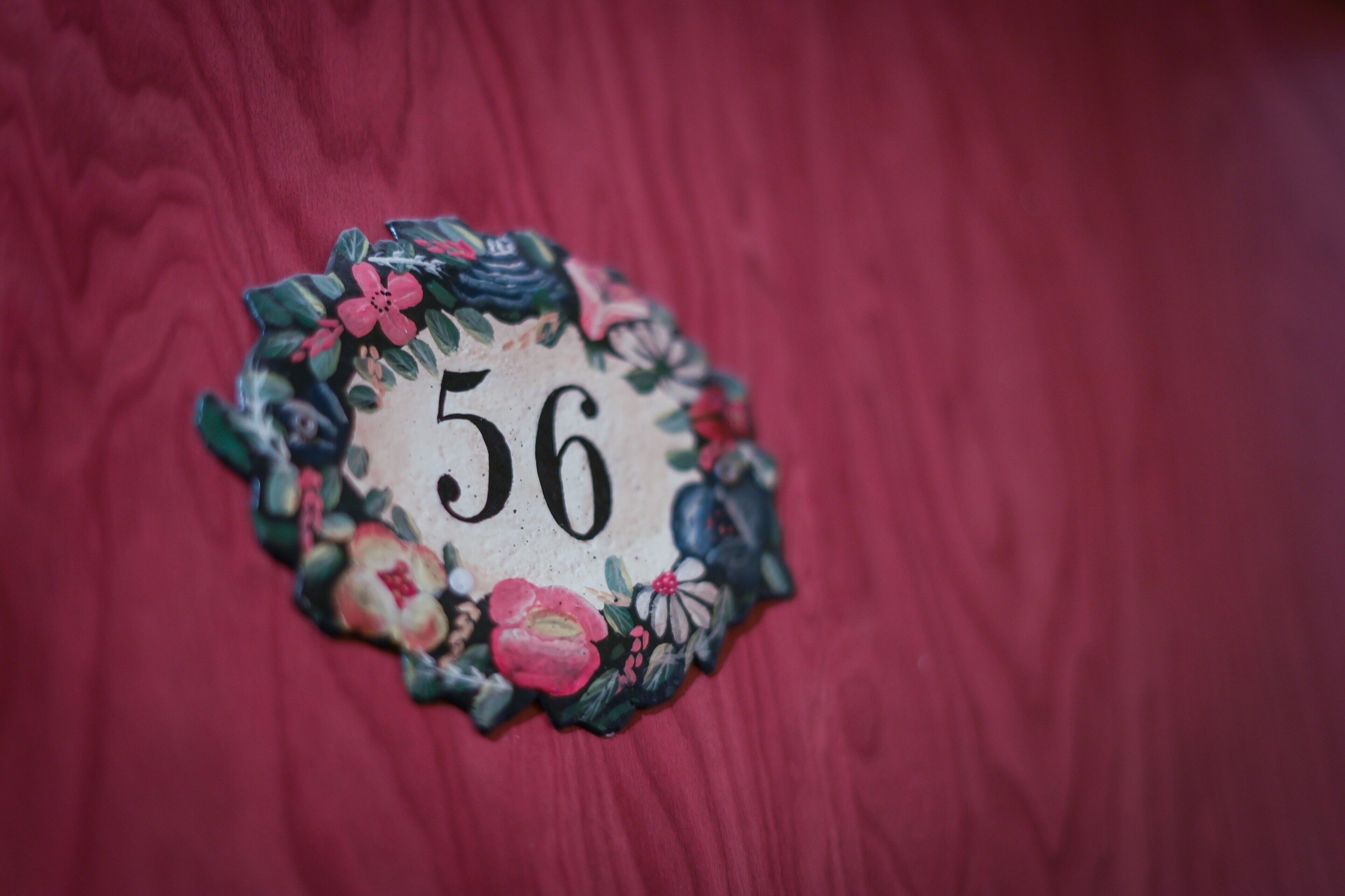 A decorative number plate with floral designs on a wooden surface.