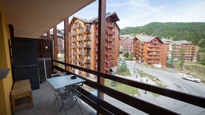 A balcony with a table and chairs, overlooking a street with buildings and a forested hill. - Apartment 'Appartemment 6 Couchages Risoul' with Mountain View and Balcony (Risoul)