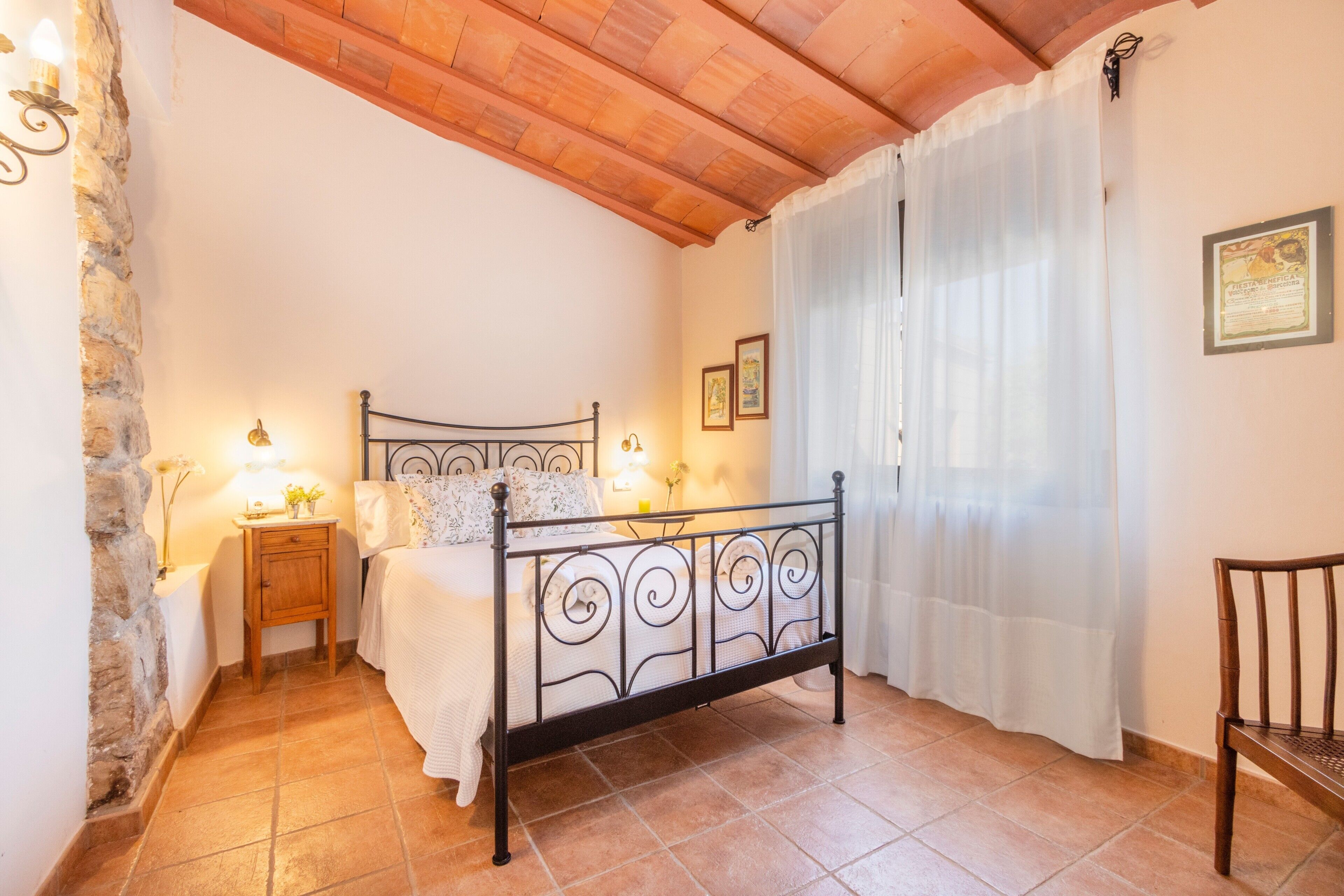 Een slaapkamer met een bed, een nachtkastje, een stoel, een stenen muur en een houten plafond.