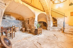 Une pièce aux murs de pierre, dotée d’une cheminée, de meubles en bois et d’un escalier.