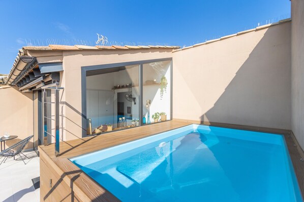 A rooftop swimming pool with a wooden deck, a sliding glass door leading to a room, and a clear blue sky. - Apartment 'Cal Comorera' with Private Pool, Wi-Fi and Air Conditioning (Massoteres)