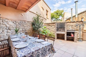 Une table installée à l’extérieur, avec des murs en pierre, un four en briques et une terrasse carrelée.