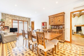 A spacious living area with a wooden dining table, comfortable seating, a stone accent wall, and a television. - Apartment 'Cal Comorera' with Private Pool, Wi-Fi and Air Conditioning (Massoteres)