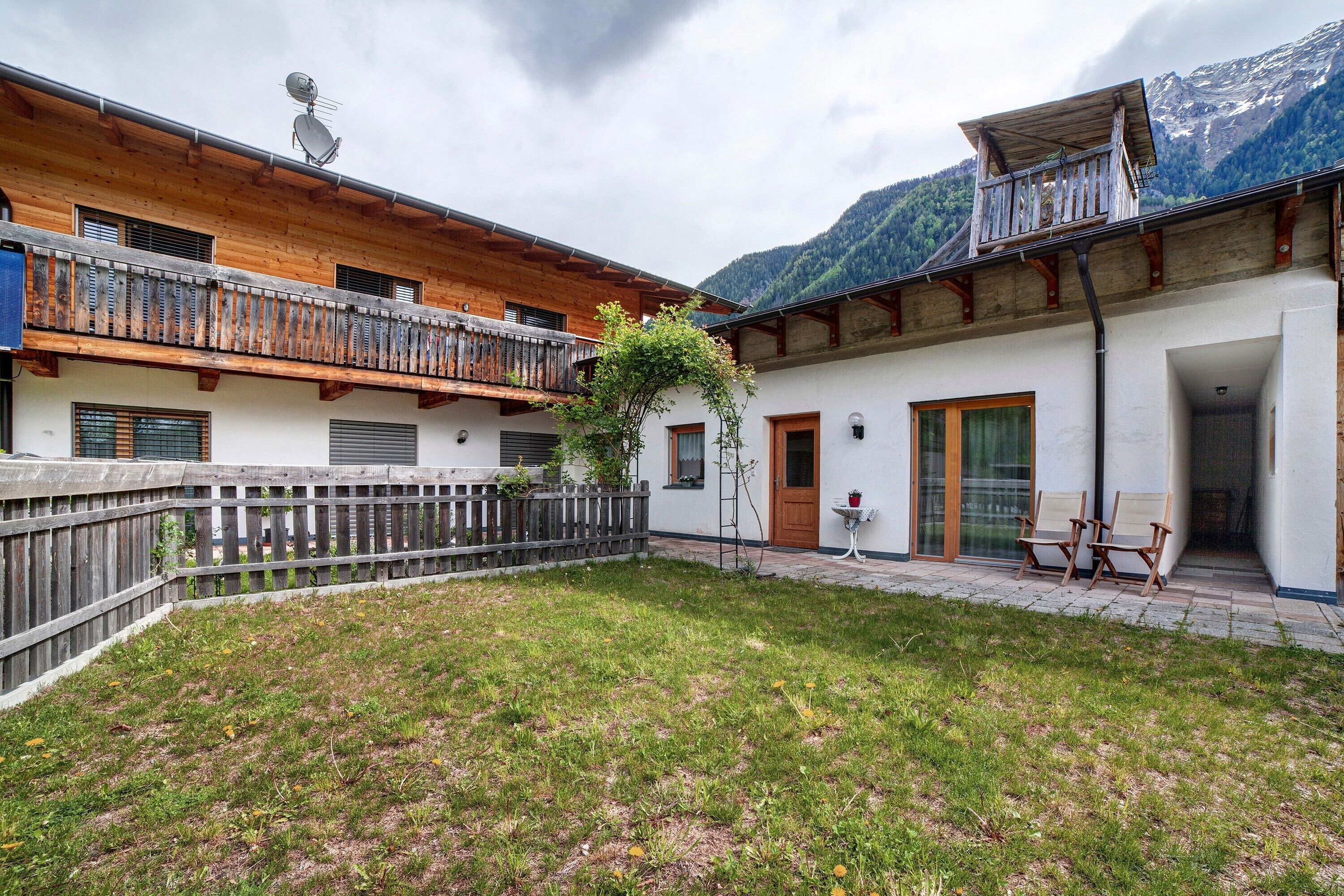 Un chalet con balcón de madera, un pequeño jardín y vistas a la montaña.