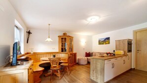 Eine kompakte Küche mit Holzschränken, einer Essecke mit einer Bank, einer kleinen Kücheninsel mit einer Mikrowelle und einem an der Wand befestigten Kruzifix.