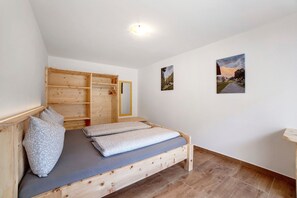 A wooden bed with a grey mattress and pillows, a wooden wardrobe, and two framed pictures on the wall.