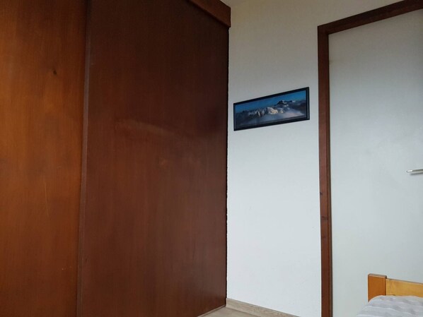 Una habitación con puerta de madera, una cama con colchón blanco y un cuadro enmarcado en la pared.