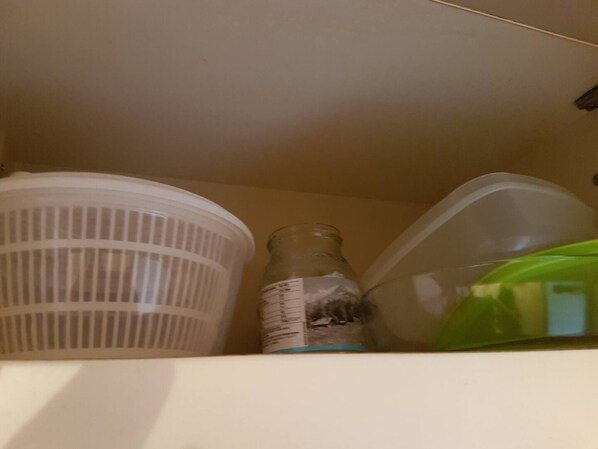 Une étagère avec un récipient en plastique, une bouteille en verre et un sac en plastique vert.