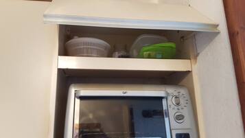 A compact kitchen with a built-in microwave oven, a white shelf above it, and a wooden vent.
