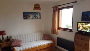 A room with a wooden sofa, a television, a window with curtains, a radiator, and a wall-mounted picture.