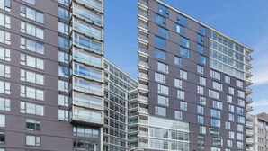 A multi-story building with a modern architectural design, featuring a mix of glass and concrete facades, and a parking lot with several cars. - Luxury 2 Bedroom at the Pinnacles on Victoria St (Wellington)
