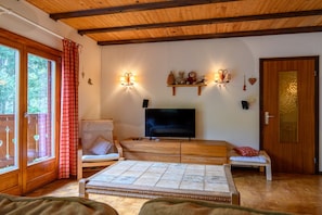 A cozy room with a wooden ceiling, a television, a sofa, a small table, and a window with curtains.