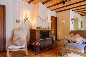 Un salon avec une cheminée, un plafond en bois, un canapé, un fauteuil et des lampes fixées au mur.