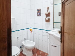 A bathroom with white tiles, a bidet, a toilet, a sink, and a mirror.