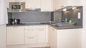 Una cocina compacta con microondas, cafetera y un lavabo con escurreplatos.