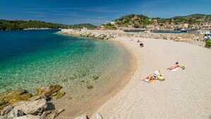A beach with clear water, a rocky shoreline, and a town in the background.