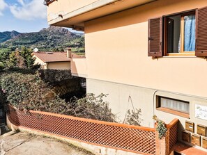A building with a red-tiled roof, a balcony with a lattice fence, and a mountain backdrop.