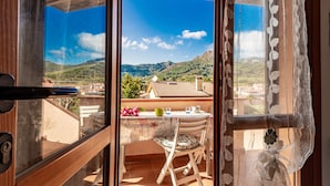 A balcony with a table, chairs, and a view of a mountainous landscape.