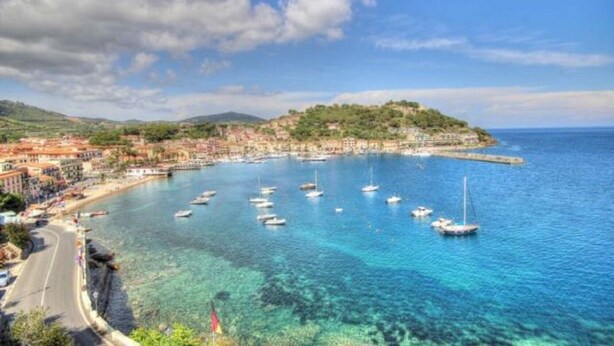 A coastal town with clear blue waters, boats, and buildings along the shore.
