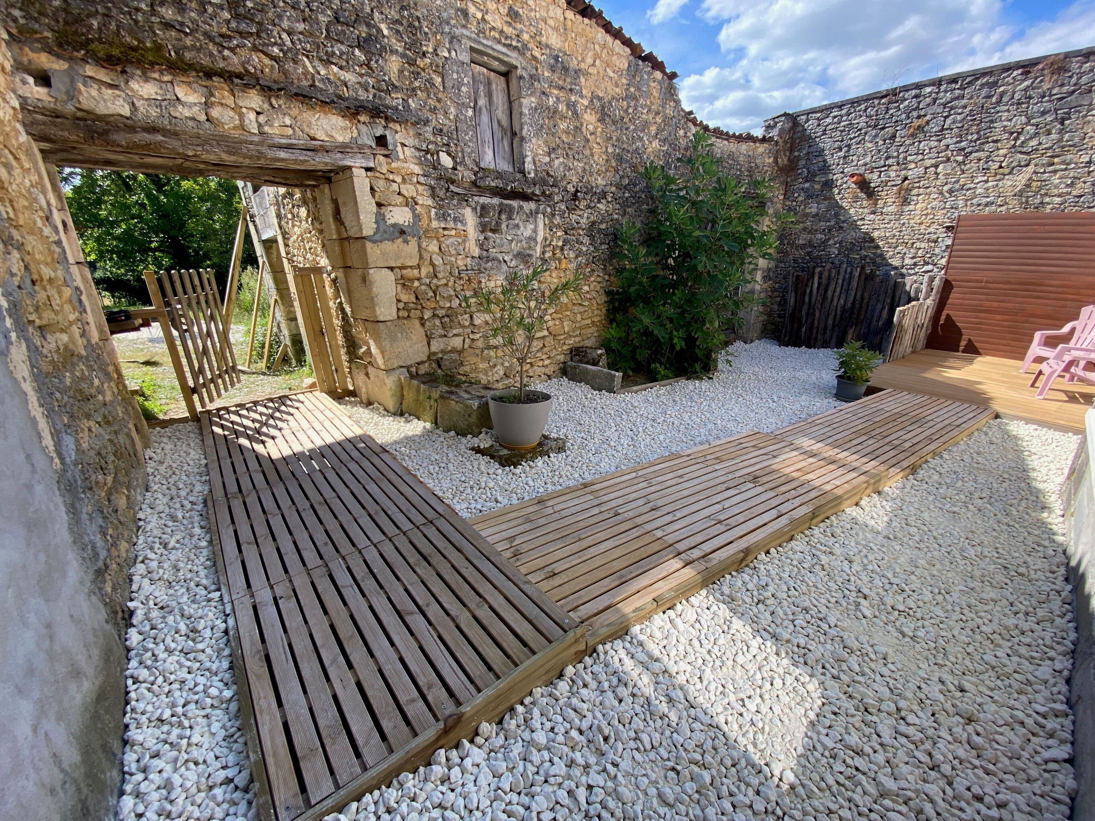 A rustic stone building with a wooden deck and gravel ground.