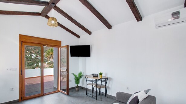 A modern living room with a sofa, a table with chairs, a TV mounted on the wall, and a sliding glass door leading to an outdoor area. - Vacation Home 'Casa Celestina' with Mountain View, Wi-Fi and Air Conditioning (Temisas)