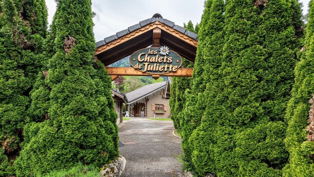 A wooden sign with 'les Chalets de Juliette' written on it, a pathway leading to a building, and coniferous trees framing the entrance. - Chalet 'Indépendant 3 Personnes' with Mountain View, Private Terrace and Wi-Fi (Alex)