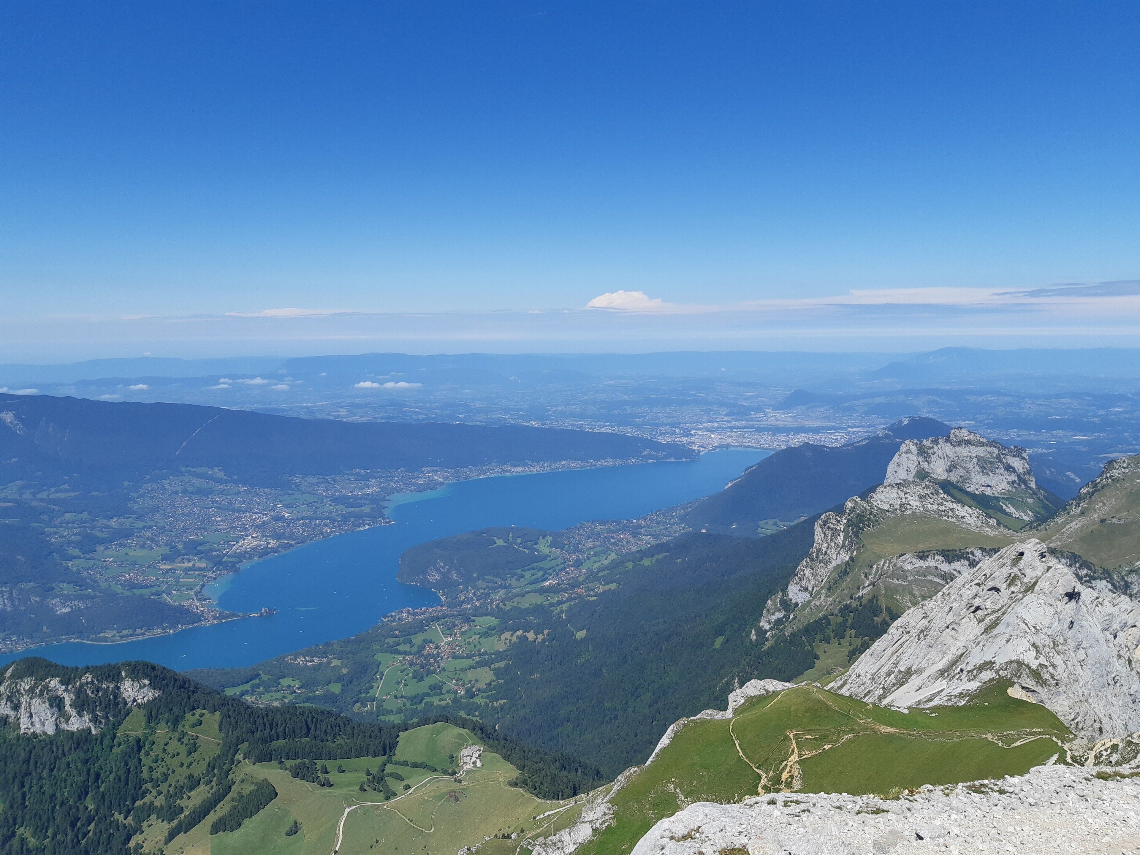 Un paysage montagneux avec un lac, un ciel dégagé et une vue sur la ville au loin.