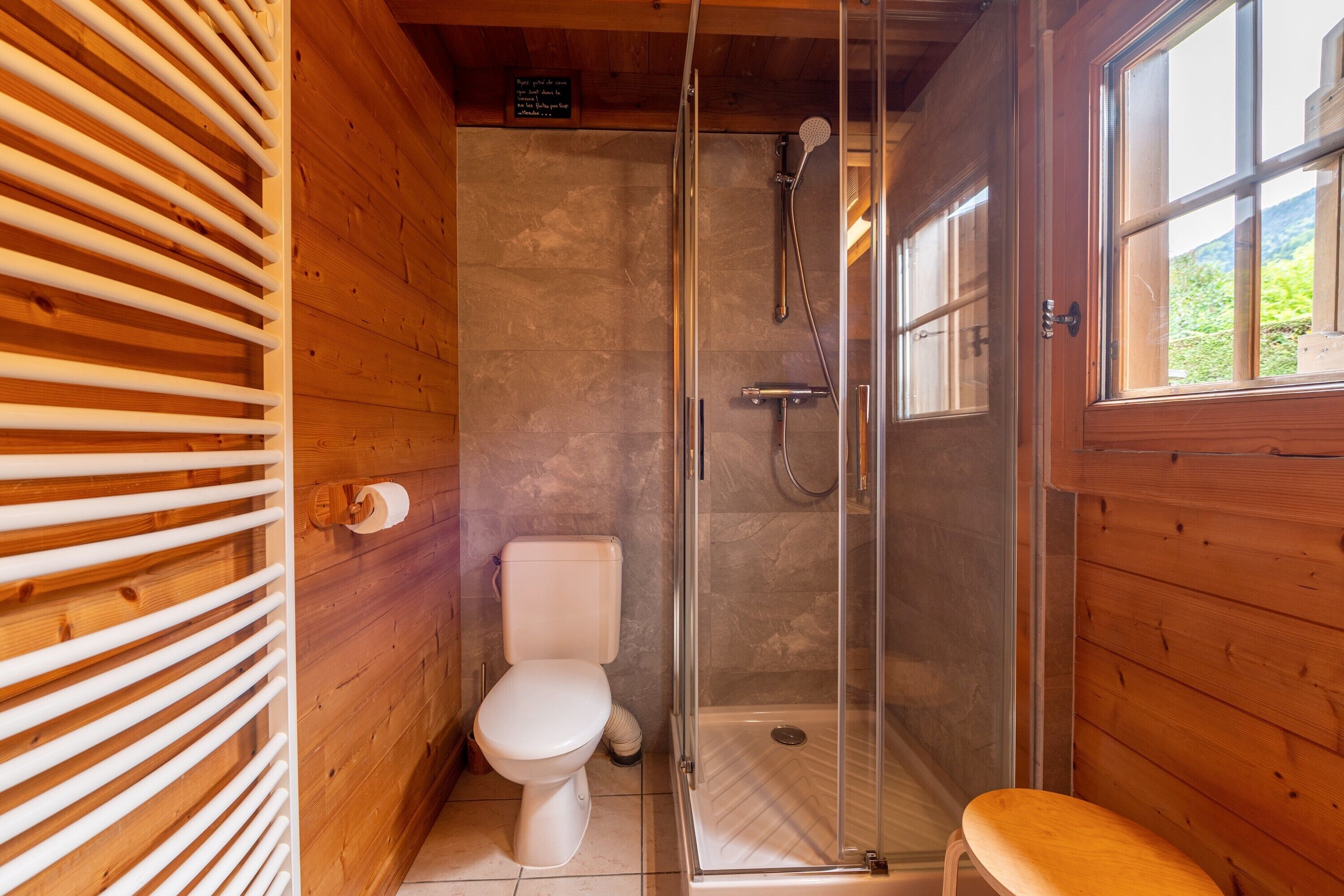 A wooden cabin bathroom with a toilet, shower, and a bench.